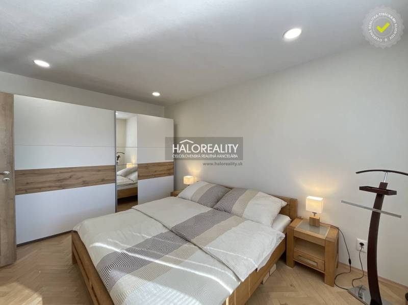 A bright bedroom in a one-room apartment with wood-patterned flooring and a built-in wardrobe.