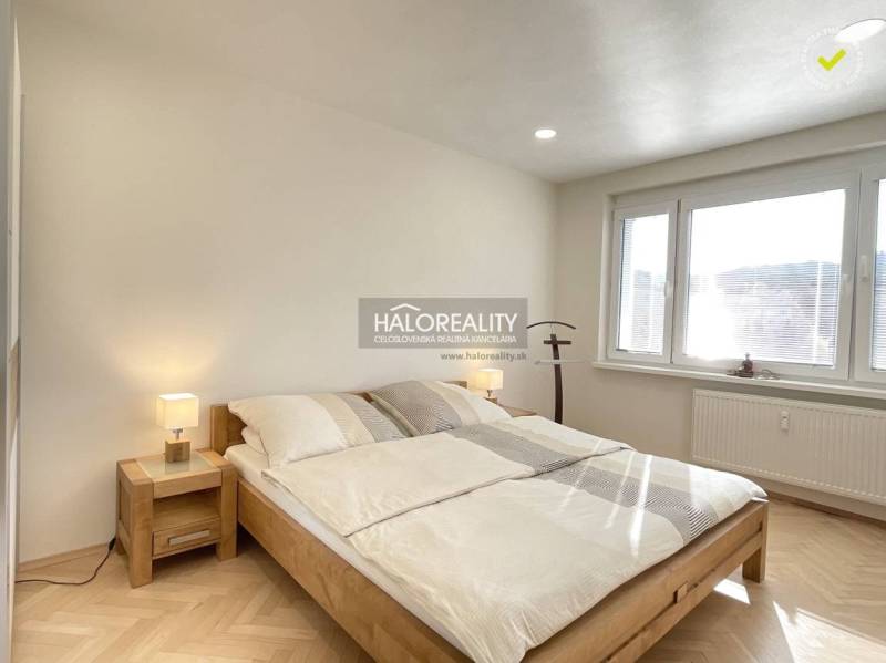 Bright bedroom in a studio apartment with wood-patterned flooring and a large window.
