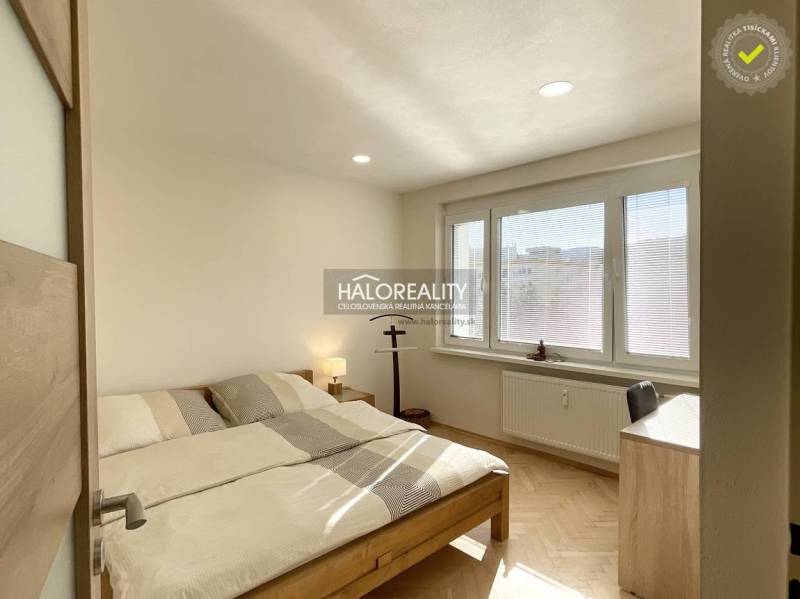 A bedroom in a studio apartment with wood-patterned flooring and large windows.