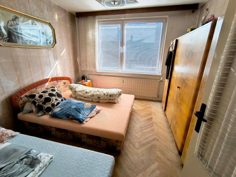 A bedroom in a 3-room apartment with a bed, a cabinet, and a floor with a wooden decor.