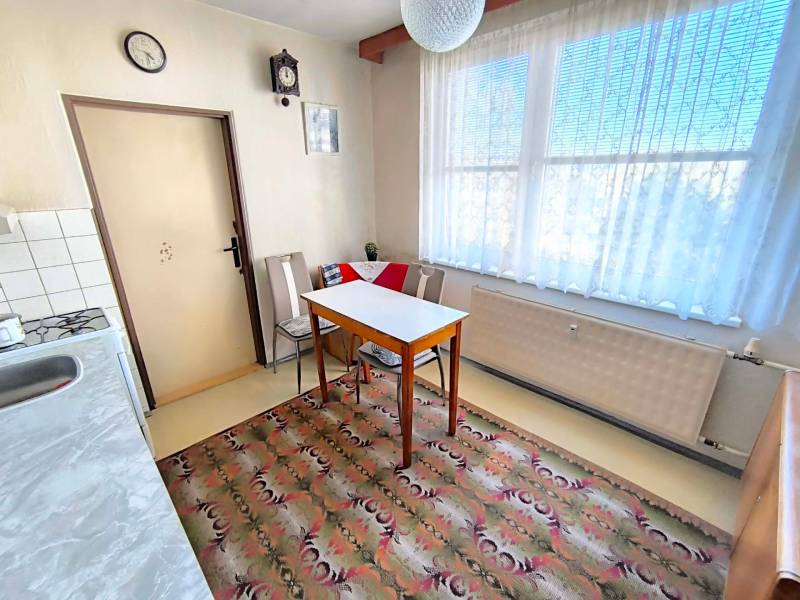 A kitchen in a 3-room apartment with a dining table, chairs, and a carpet.