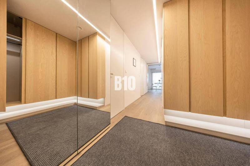 A hallway in a 3-room apartment with a wooden decor floor and a mirror.