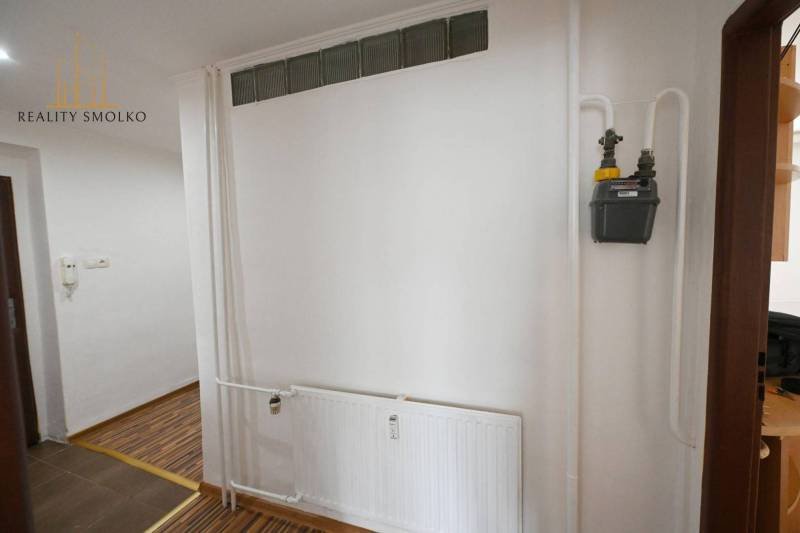An interior with a white wall, a radiator, and a wooden decor floor in a 2-room apartment.
