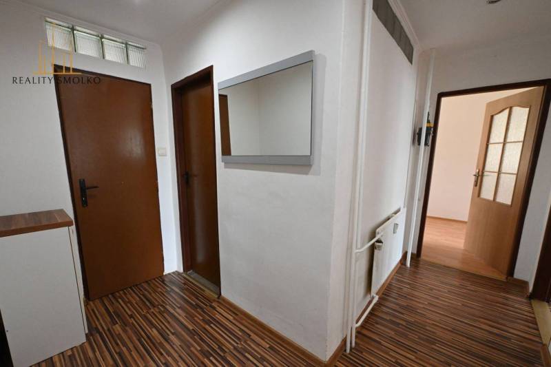 A hallway in a 2-room apartment with a wooden-patterned floor and a mirror on the wall.