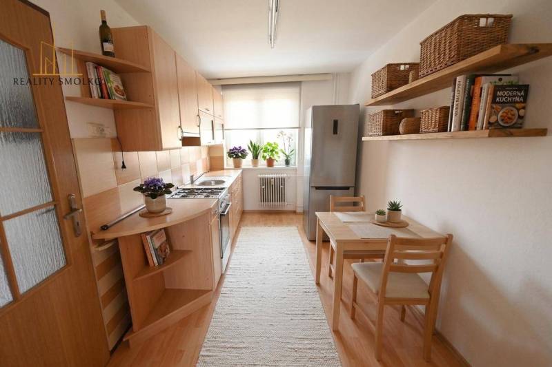 A kitchen in a 2-room apartment with a wooden decor floor, a dining table, and shelves.