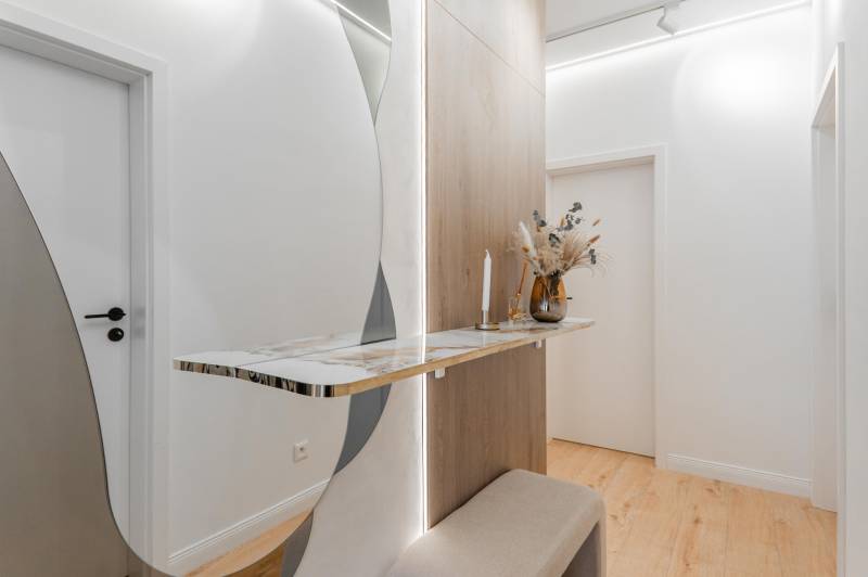 A hallway in a 3-room apartment with a minimalist table, mirror, and floor with a wooden decor.