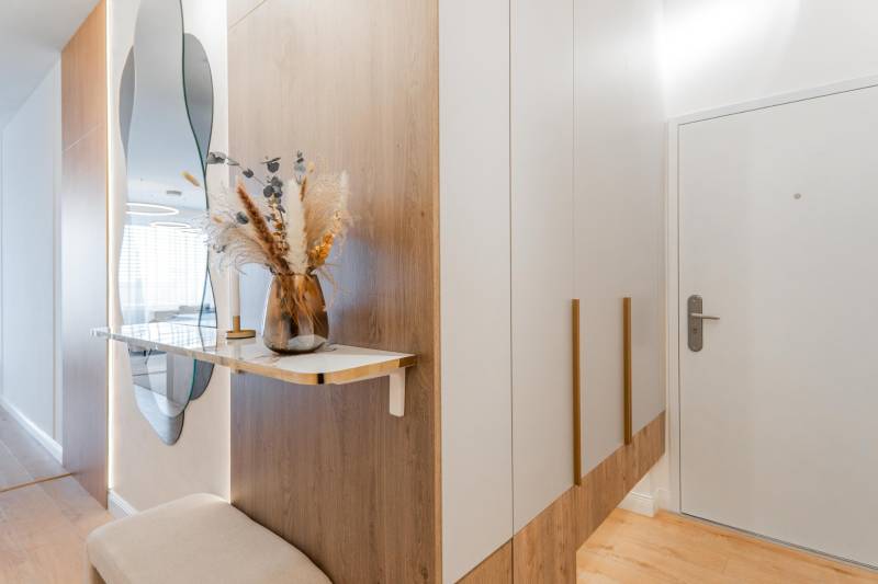 Entrance hallway with a mirror, wardrobe, and decoration in a 3-room apartment with a wooden decor floor.