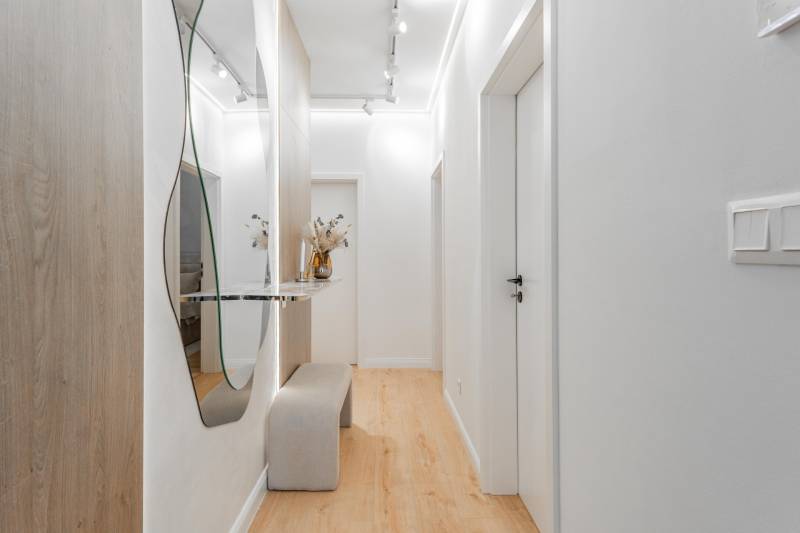 A bright hallway with a mirror, a bench, and a wooden decor floor in a 3-room apartment.