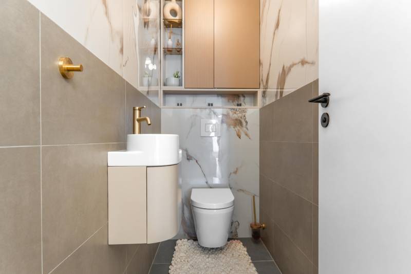 A toilet with a sink, a gold faucet, and marble-patterned tiles in a three-room apartment.