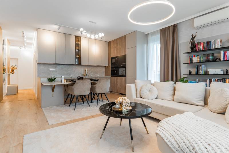 A stylish living room with a kitchen in a 3-room apartment, light shades, wooden decor flooring.