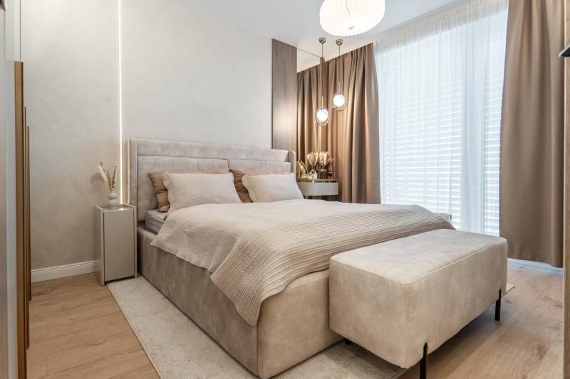 Bright bedroom with a comfortable bed, beige curtains, and a wood-patterned floor.