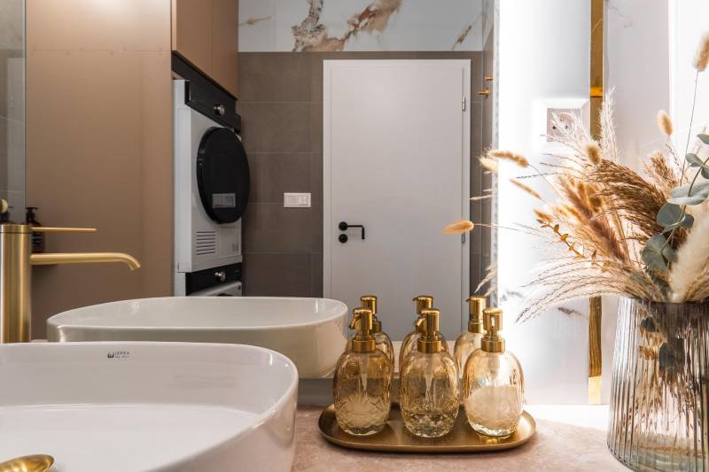 Bathroom with a sink, gold dispensers, and decorative natural decorations in a 3-room apartment.