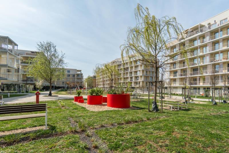 The exterior of apartment buildings in Bratislava - Ružinov with trees and benches.