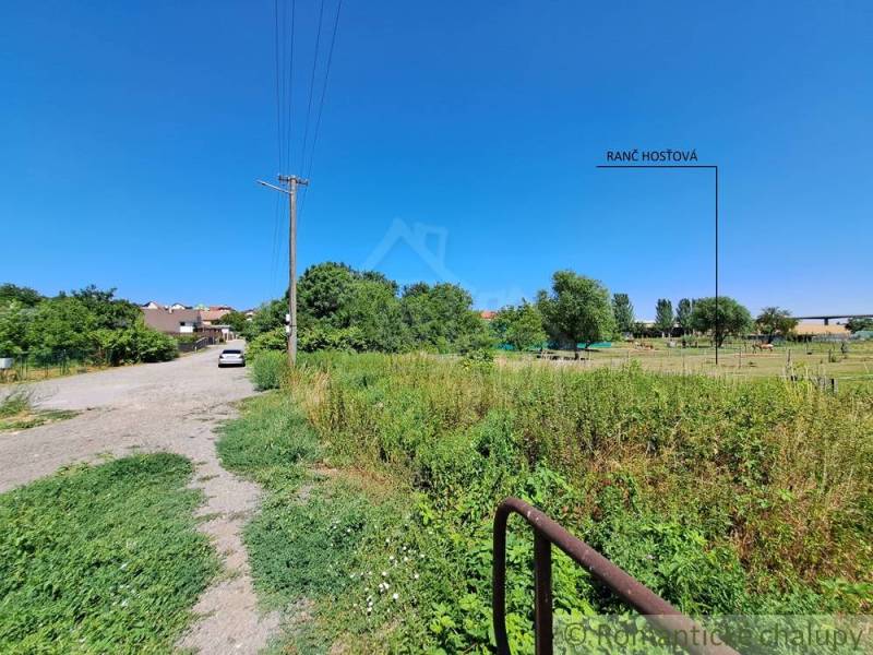 The path leads to the plots - housing in Hosťová with a view of greenery and houses.