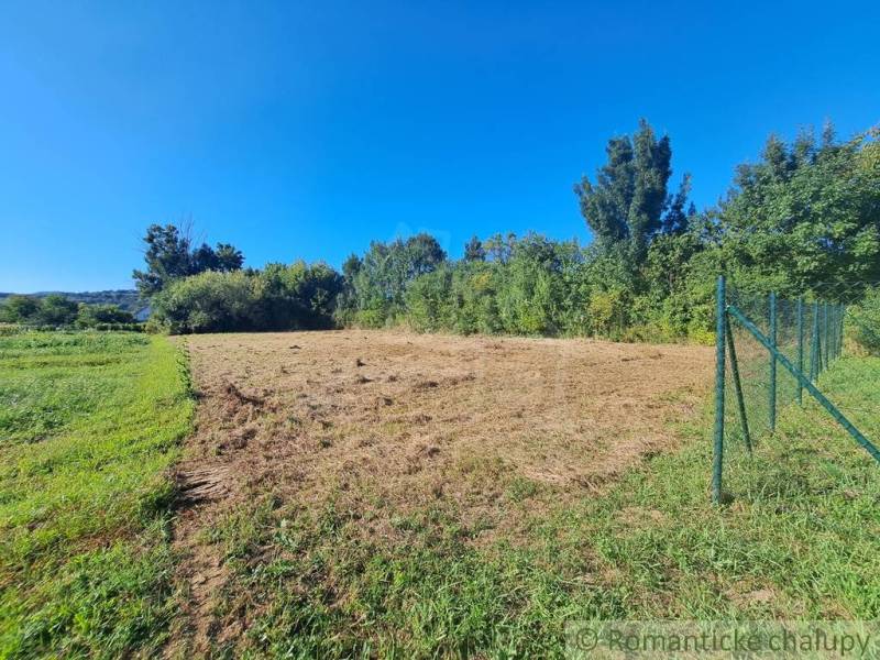 A plot for living in Hosťová with fencing and surrounding greenery under a blue sky.