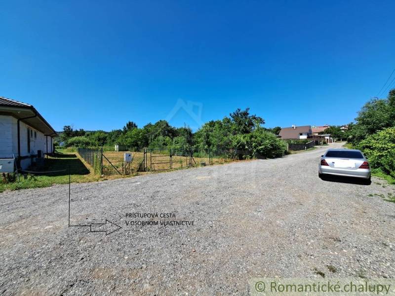 Land - housing in Hosťová: gravel road, fenced plot, parked car next to it.
