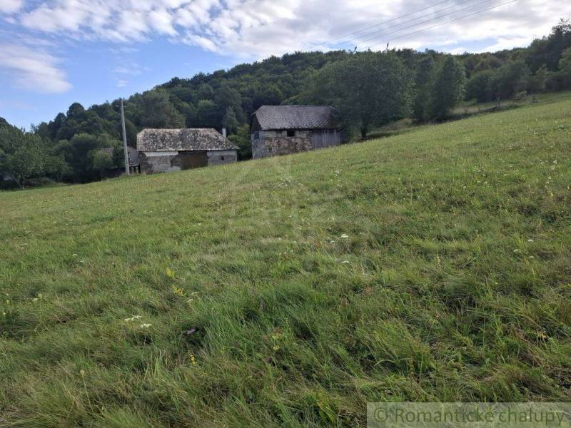 A grassy slope with buildings in the background, surrounded by nature in Horný Tisovník, ideal for residential land.
