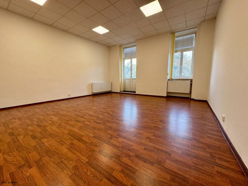 An empty office with wood-patterned flooring and large windows.