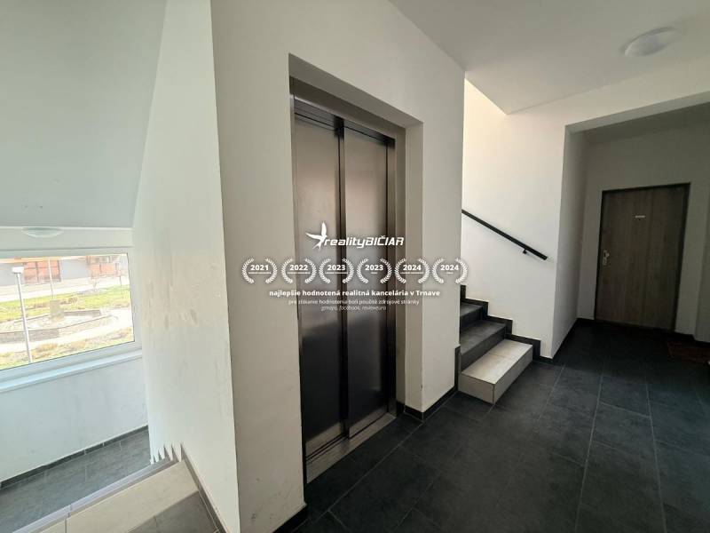 A hallway with an elevator and staircase in a 2-room apartment, flooring with a wooden decor.
