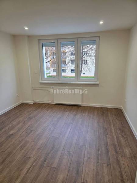 A spacious room in a 3-room apartment with a wood-patterned floor and large windows.