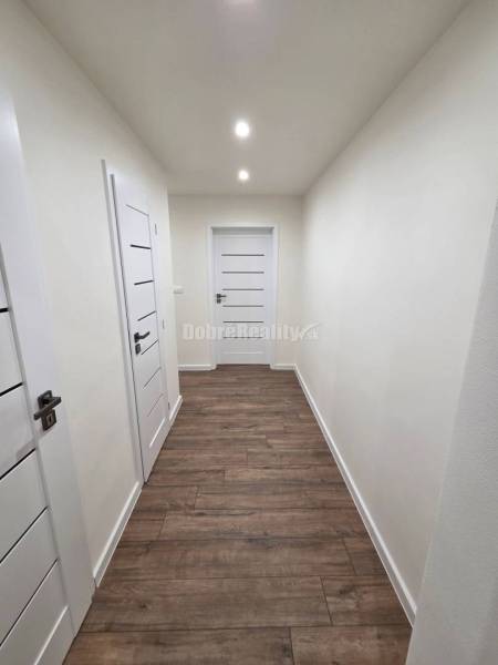 A hallway in a 3-room apartment with white doors and a wooden-patterned floor.