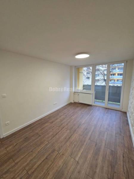 A room with a wooden decor floor and large windows in a 3-room apartment.