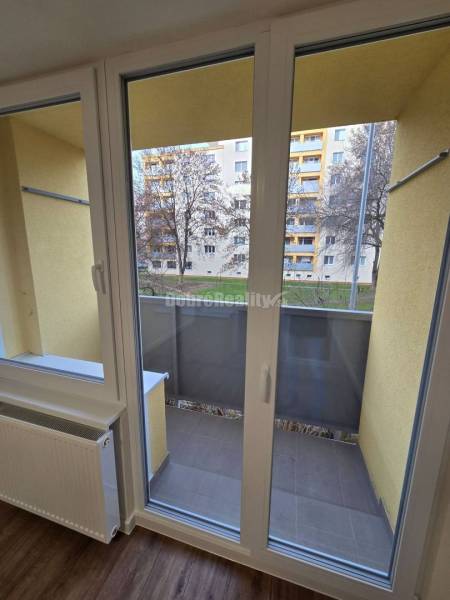 French window in a 3-room apartment with a wooden decor floor and a view of the balcony.
