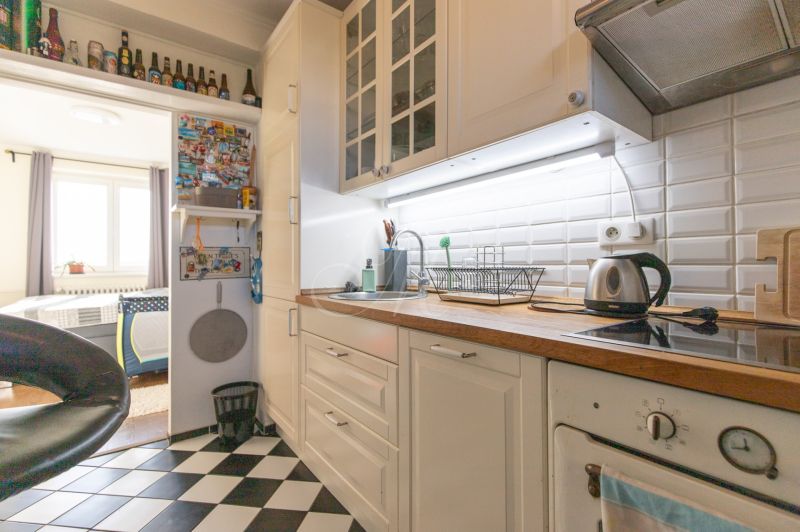 A kitchen in a 2-room apartment with white cabinets, black and white checkered tiles.