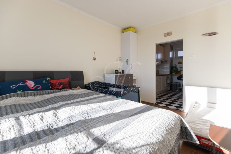 Bedroom in a 2-room apartment with a bed and a passage to the kitchen. Floor with wood decor.