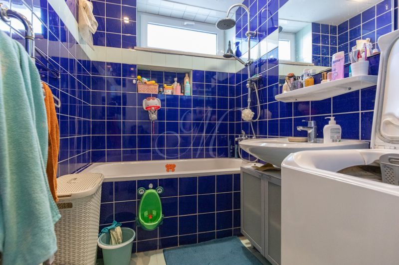 A bathroom with blue tiles, a sink, a bathtub, and a washing machine in a 2-room apartment.