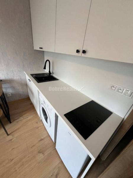 A kitchenette in a studio apartment with white cabinets and a wood-patterned floor.