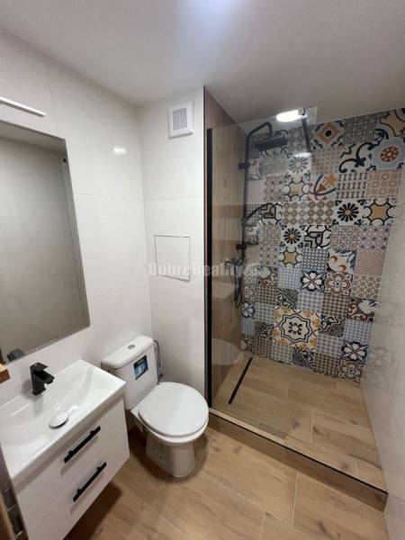 A bathroom in a studio apartment with a modern shower and a wooden decor floor.