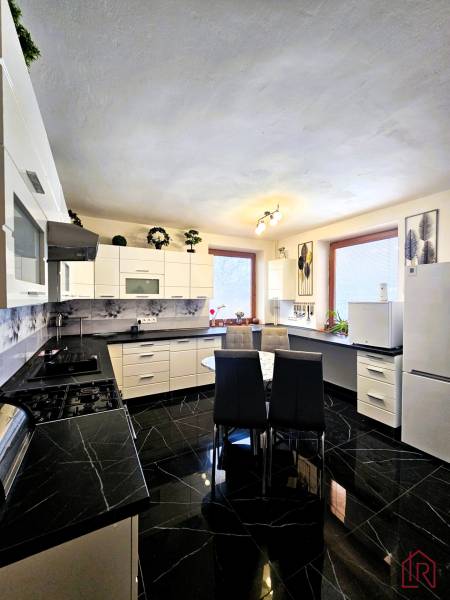A kitchen in a family house with black glossy tiles and white furniture.