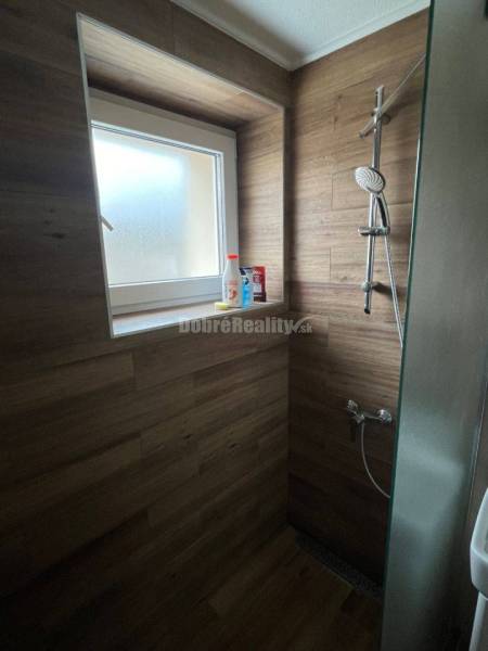 Shower corner in a 2-room apartment with wood decor tiles and a window.