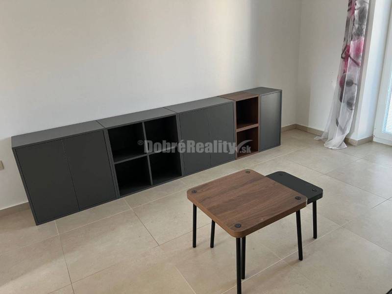 Living room in a two-room apartment with tiles, a table, and a dark cabinet.