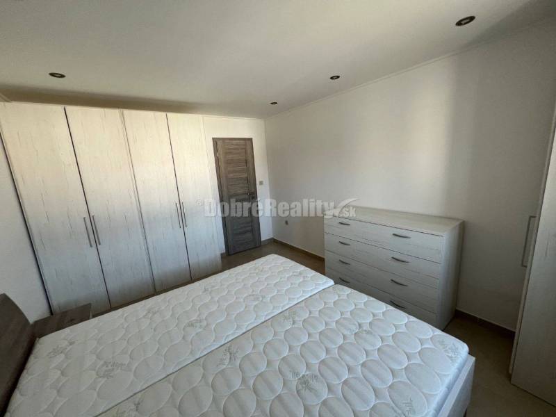 Bedroom in a 2-room apartment with white furniture and a wood-patterned floor.