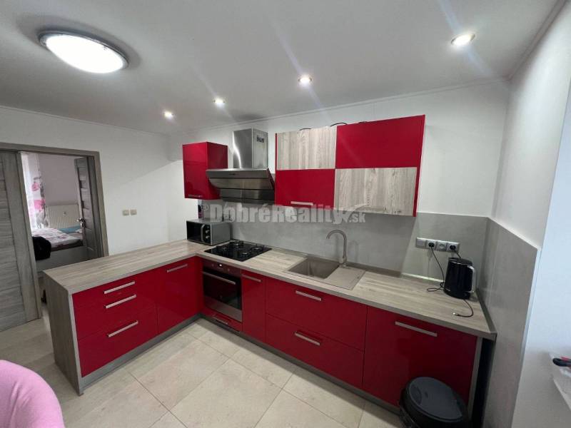 A kitchen with red cabinets and a wood-patterned floor in a two-room apartment.