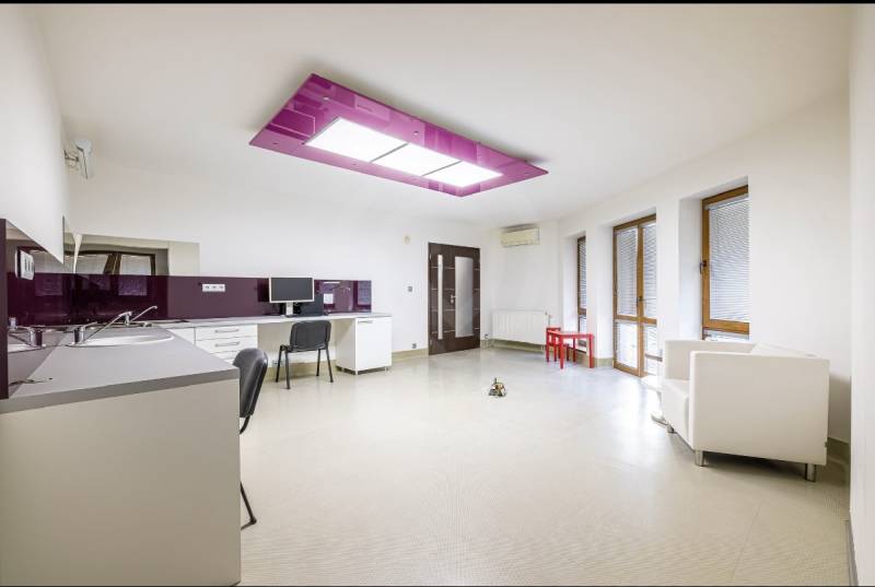 A kitchen with white furniture, a purple ceiling panel, and light walls in a family house.