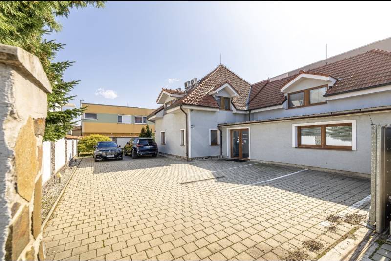 A family house in Bratislava-Vrakuňa, on Podpriehradná Street, with a paved parking lot and parked cars.