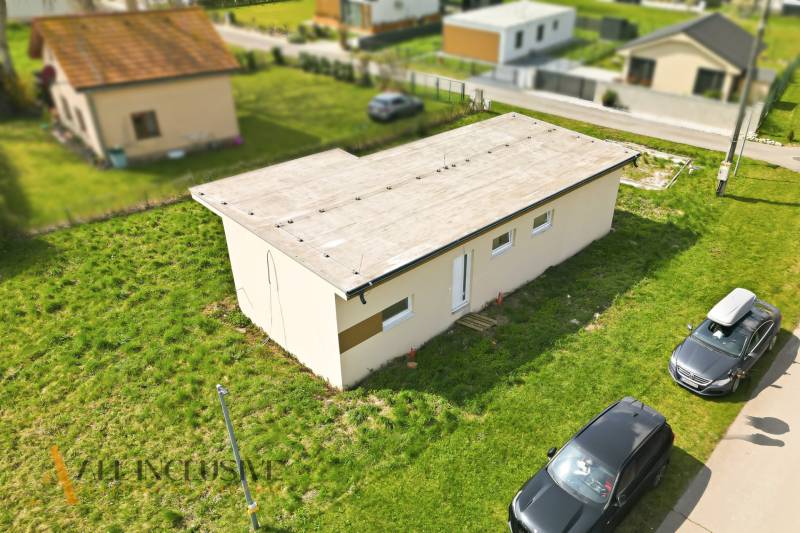 A cottage in Vojka nad Dunajom with a flat roof and cars parked on the grassy area.