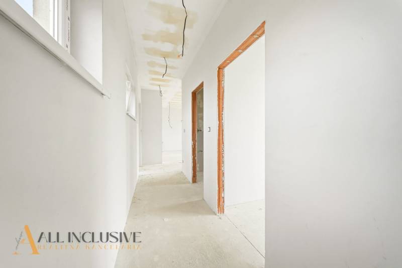 A bright hallway in a cottage with a raw floor, white walls, visible cables.