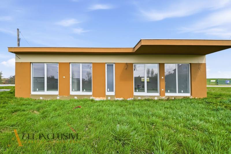 A cottage in Vojka nad Dunajom with large windows and a flat roof, surrounded by a grassy area.