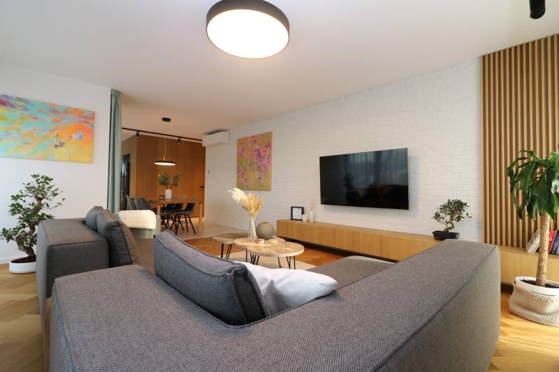 Living room in a 4-room apartment with a wooden decor floor, gray sofa, and plants.