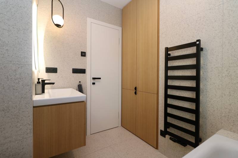 Bathroom with a cabinet, white sink, and black ladder radiator in a 4-room apartment.