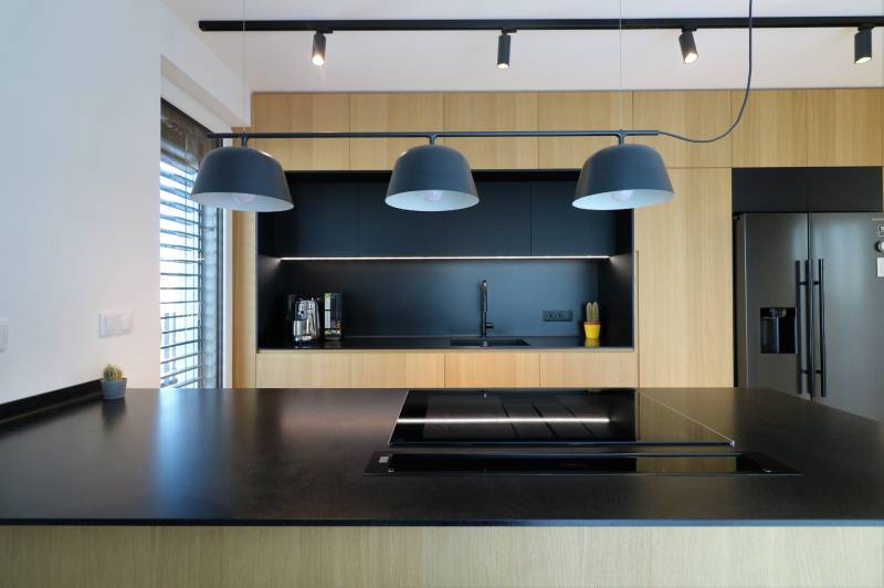 A kitchen in a 4-room apartment with black and wooden elements, pendant lighting.