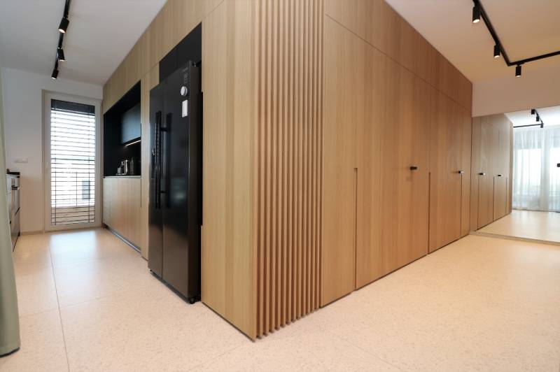 A kitchen in a 4-room apartment with wood decor, a black refrigerator, and white tiles.