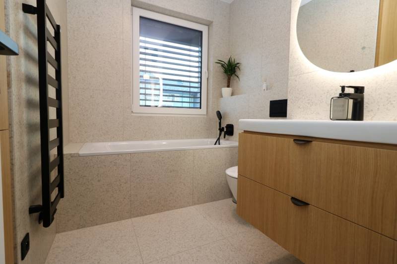 A bathroom in a 4-room apartment with a bathtub, sink, and wooden cabinet decor.