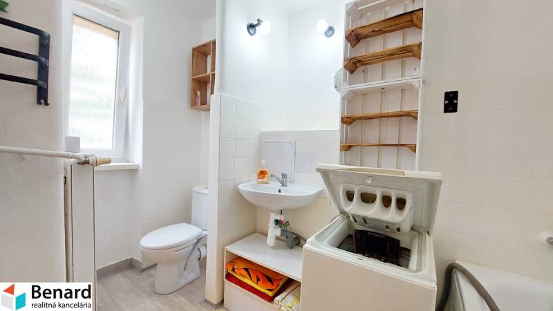 A bathroom in a 2-room apartment with a washing machine, a sanitizer, and a towel rack.