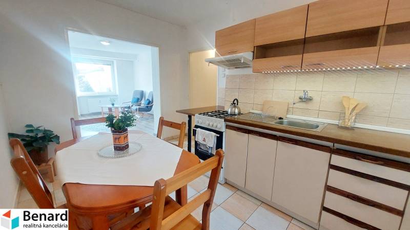A kitchen in a 2-room apartment with a seating area, light flooring, and a dining table.
