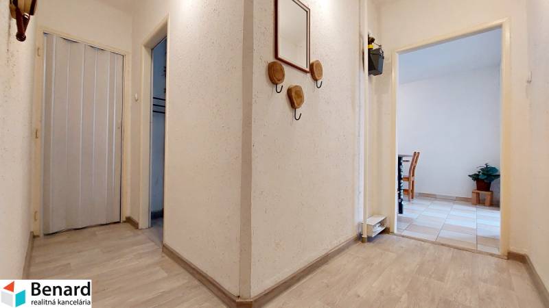 A hallway in a 2-room apartment with white walls and a wooden decor floor.
